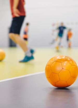orange futsal soccer ball on indoor training pitch. young players on sports practice running balls in blurred background. school sports class for kids